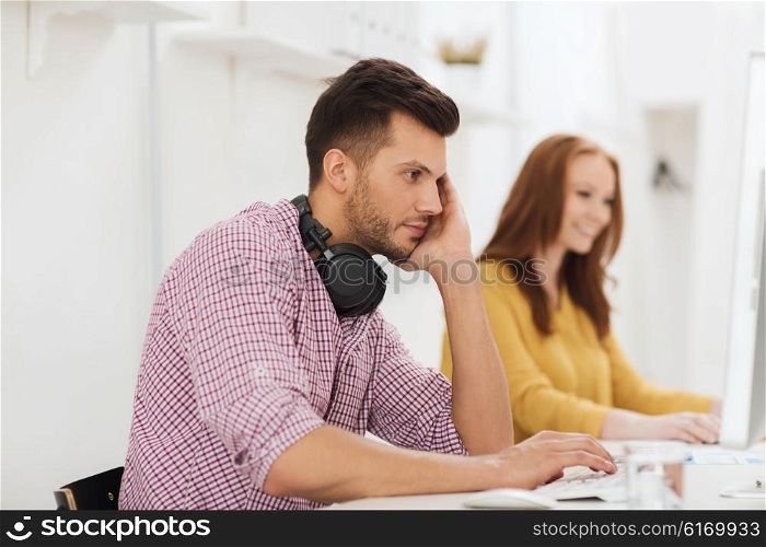 business, startup, education, technology and people concept - creative team or students with headphones and computer at office