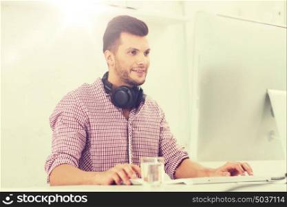 business, startup, education, technology and people concept - happy creative man or student with headphones and computer at office. creative man with headphones and computer