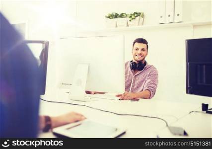business, startup, education, technology and people concept - happy creative man or student with headphones and computer at office. creative man with headphones and computer