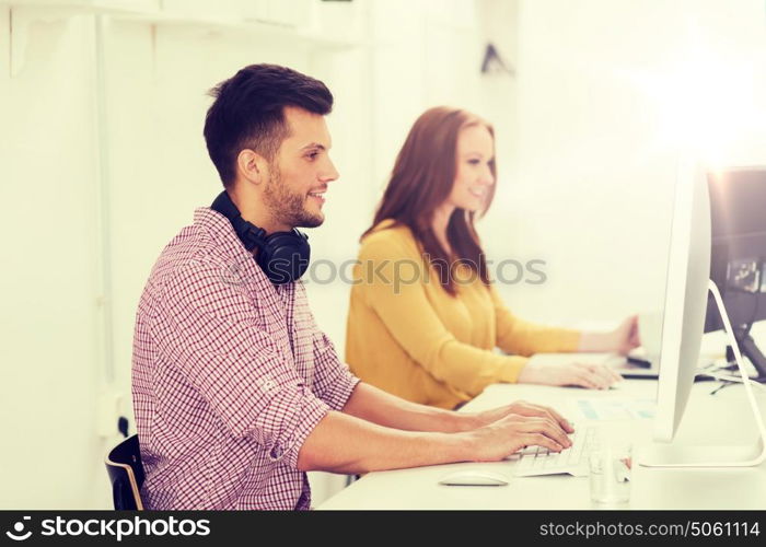 business, startup, education, technology and people concept - happy creative team or students with headphones and computer at office. creative team with headphones and computer