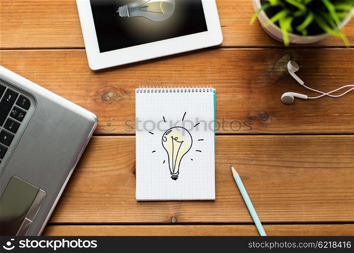 business, startup, idea and technology concept - close up of notebook with light bulb, laptop and tablet pc computer with