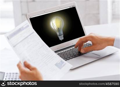 business, startup, idea, technology and people concept - businessman with light bulb on laptop computer screen working at office