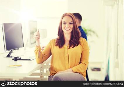 business, startup, people and break concept - happy businesswoman drinking coffee or tea at office. happy woman drinking coffee or tea at office