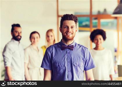 business, startup, people and teamwork concept - happy young man with beard and bow tie over creative team in office