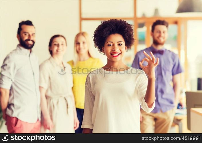 business, startup, people, gesture and teamwork concept - happy young african woman showing ok hand sig over international creative team in office