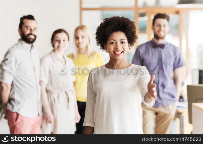 business, startup, people, gesture and teamwork concept - happy young african woman greeting by handshake over international creative team in office