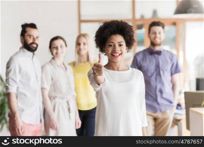 business, startup, people, gesture and teamwork concept - happy young african woman showing thumbs up over international creative team in office