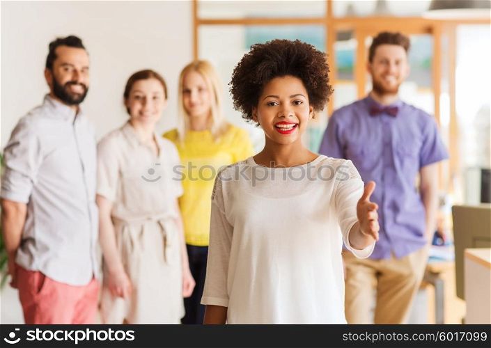 business, startup, people, gesture and teamwork concept - happy young african woman greeting by handshake over international creative team in office