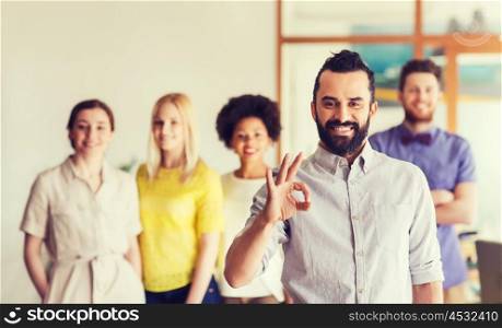 business, startup, people, gesture and teamwork concept - happy young man with beard showing ok hand sign over creative team in office