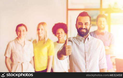 business, startup, people, gesture and teamwork concept - happy young man with beard showing thumbs up over creative team in office