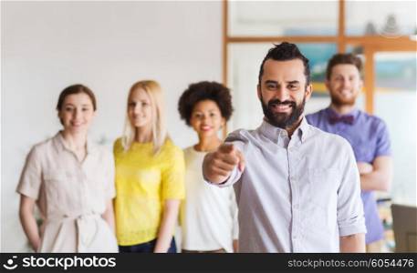 business, startup, people, gesture and teamwork concept - happy young man with beard pointing finger at you over creative team in office