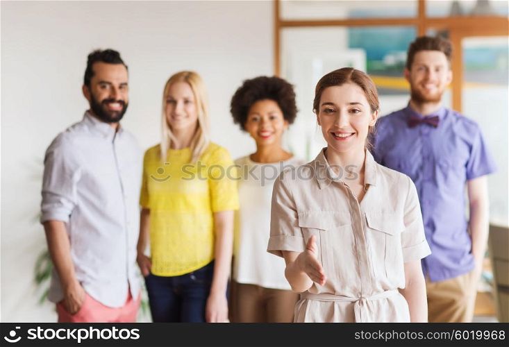 business, startup, people, gesture and teamwork concept - happy young woman greeting by handshake over creative team in office