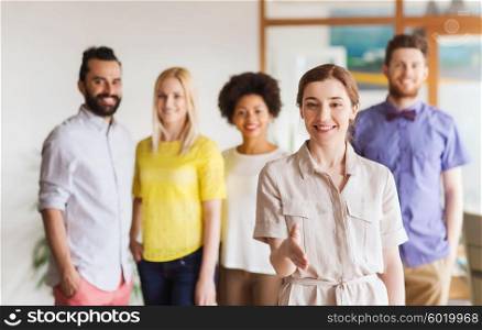 business, startup, people, gesture and teamwork concept - happy young woman greeting by handshake over creative team in office