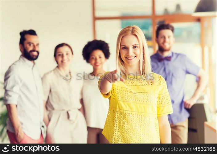 business, startup, people, gesture and teamwork concept - happy young woman pointing finger at you over creative team in office
