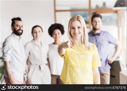 business, startup, people, gesture and teamwork concept - happy young woman pointing finger at you over creative team in office