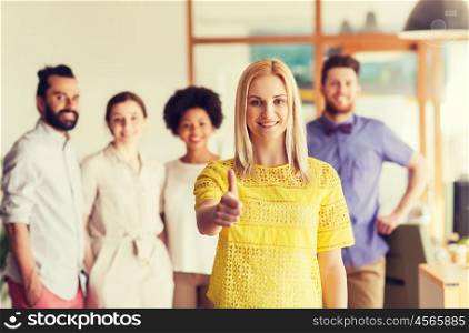 business, startup, people, gesture and teamwork concept - happy young woman showing thumbs up over creative team in office