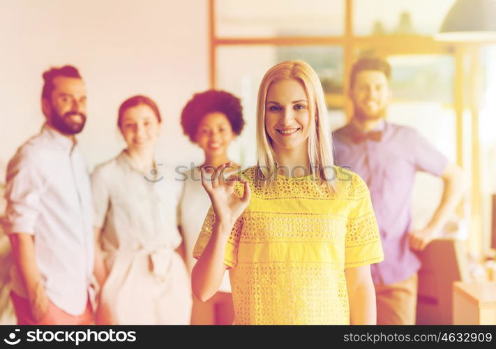 business, startup, people, gesture and teamwork concept - happy young woman showing ok hand sig over creative team in office