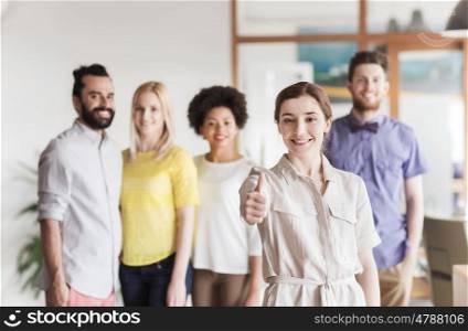 business, startup, people, gesture and teamwork concept - happy young woman showing thumbs up over creative team in office
