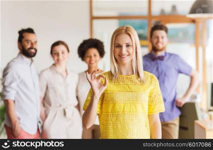 business, startup, people, gesture and teamwork concept - happy young woman showing ok hand sig over creative team in office
