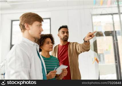 business, startup, planning and people concept - happy creative team looking at office glass board. creative team looking at office glass board