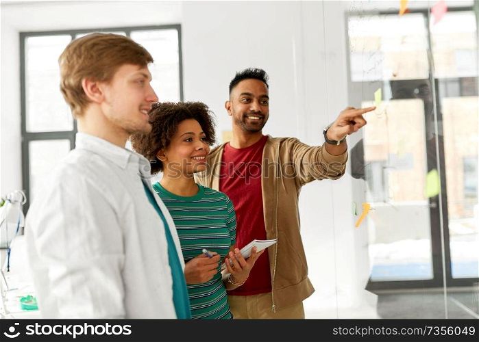 business, startup, planning and people concept - happy creative team looking at office glass board. happy creative team looking at office glass board
