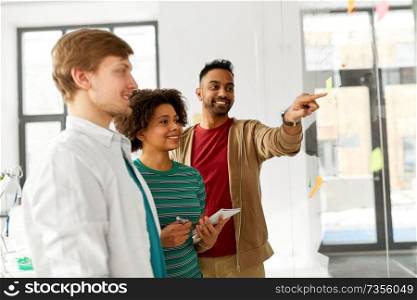business, startup, planning and people concept - happy creative team looking at office glass board. happy creative team looking at office glass board
