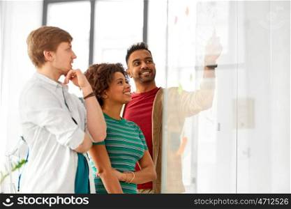 business, startup, planning and people concept - happy creative team writing on glass board at office. creative team writing on glass board at office. creative team writing on glass board at office