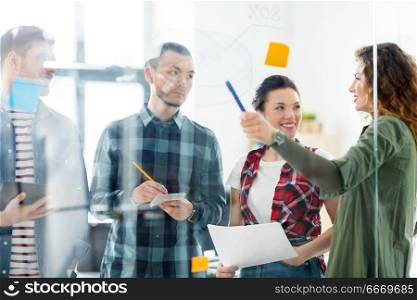 business, startup, planning and people concept - happy creative team writing on glass board at office. creative team writing on glass board at office. creative team writing on glass board at office