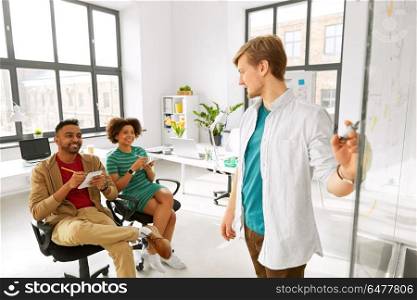 business, startup, planning and people concept - man showing scheme on glass board to creative team at office conference or presentation. man showing scheme to creative team at office. man showing scheme to creative team at office