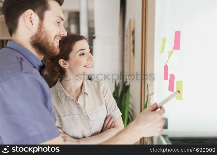 business, startup, planning, management and people concept - happy creative team with stickers on office glass board