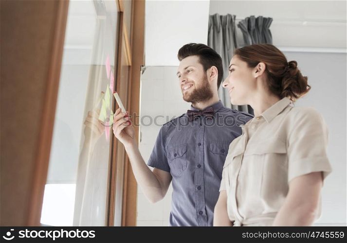 business, startup, planning, management and people concept - happy creative team with stickers on office glass board
