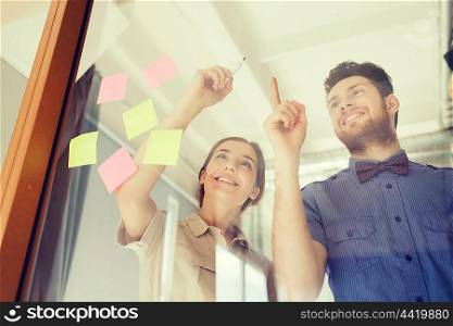 business, startup, planning, management and people concept - happy creative team writing or drawing something on blank office glass board