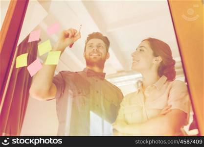 business, startup, planning, management and people concept - happy creative team writing or drawing something on blank office glass board