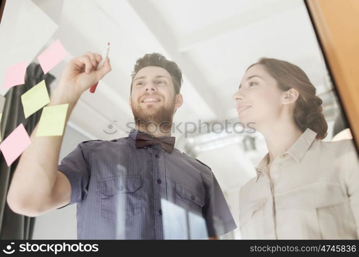 business, startup, planning, management and people concept - happy creative team writing or drawing something on blank office glass board