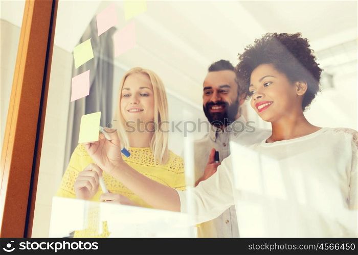 business, startup, planning, management and people concept - happy international creative team writing on stickers at office glass board