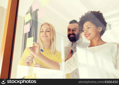 business, startup, planning, management and people concept - happy international creative team writing on stickers at office glass board