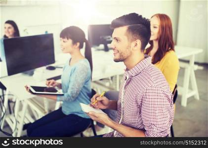 business, startup, planning, strategy and people concept - happy creative team and man with notebook and pencil taking notes on conference or seminar at office. creative team on conference or seminar at office