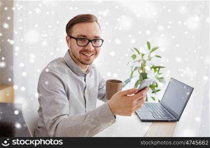 business, startup, technology and people concept - happy businessman or creative male worker texting on smarphone and drinking coffee at home office over snow