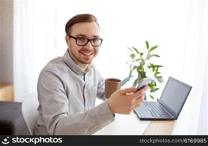 business, startup, technology and people concept - happy businessman or creative male worker texting on smarphone and drinking coffee at home office