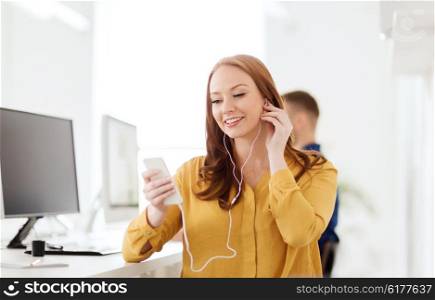 business, startup, technology and people concept - happy businesswoman or creative worker with earphones listening to music on smartphone at office