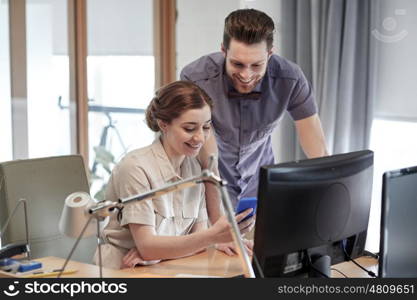 business, startup, technology and people concept - happy creative team with smartphone and computer in office