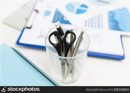 business, stationery and office supply concept - close up of organizer with scissors and pens over charts on table