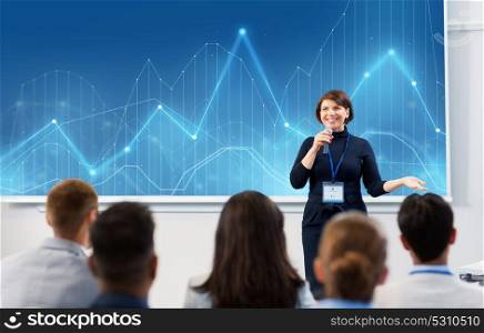 business, statistics and people concept - smiling businesswoman or lecturer with microphone and diagram chart on projection screen talking to group of students at conference presentation or lecture. group of people at business conference or lecture