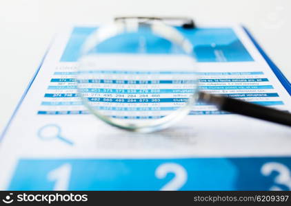 business, statistics, economy, finance and research concept - close up of financial report document and magnifying glass