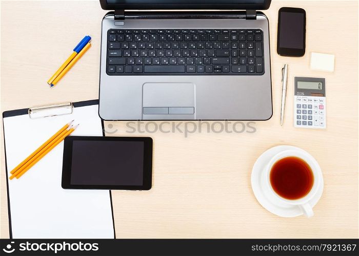 business still life - above view of laptop, tablet PC, smartphone, clipboard, calculator, cup of tea, pen and pencil on office table