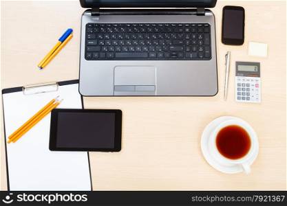 business still life - above view of laptop, tablet PC, smartphone, clipboard, calculator, cup of tea, pen and pencil on office table