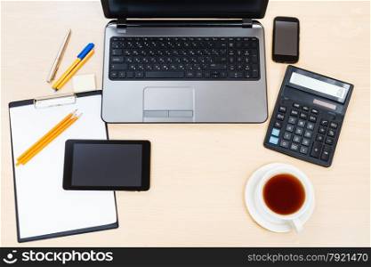business still life - top view of laptop, tablet PC, smartphone, clipboard, financial calculator, cup of tea, pen and pencil on office table