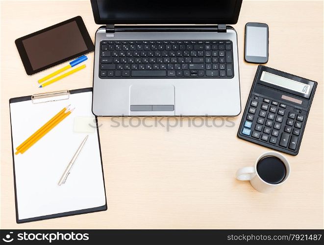 business still life - top view of laptop, tablet PC, smartphone, clipboard, financial calculator, mug of coffee, pen and pencil on office table