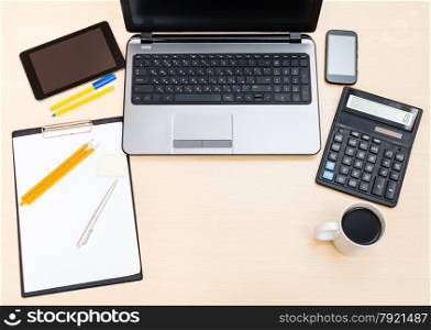 business still life - top view of laptop, tablet PC, smartphone, clipboard, financial calculator, mug of coffee, pen and pencil on office table