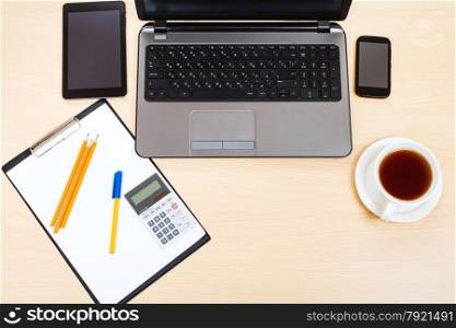 business still life - top view of workplace with laptop, tablet PC, smartphone, clipboard, calculator, cup of tea, pen and pencil on office table